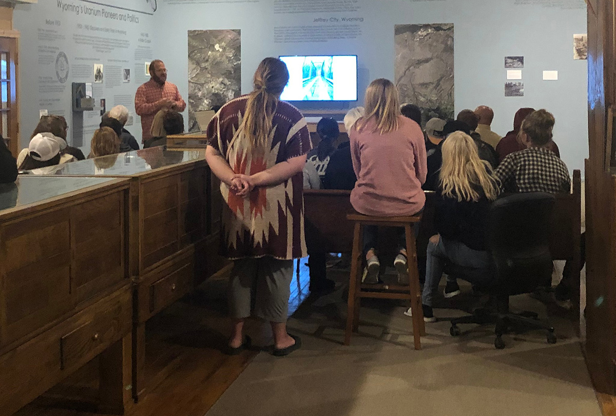 color image of group of people listening to a speaker with a projector screen in the background